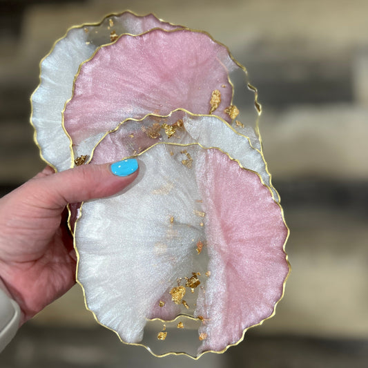 Hand holding a set of pink and white resin coasters with gold leaf and metallic gold edging