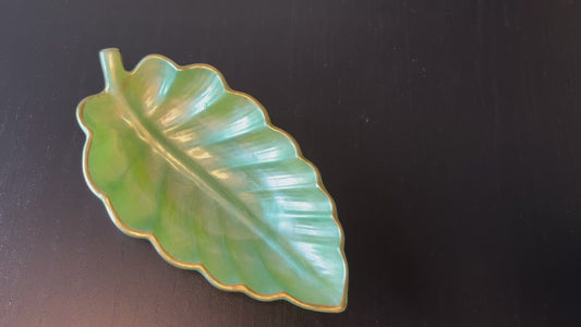 Video of small light green resin leaf tray with gold trim placing items to show size